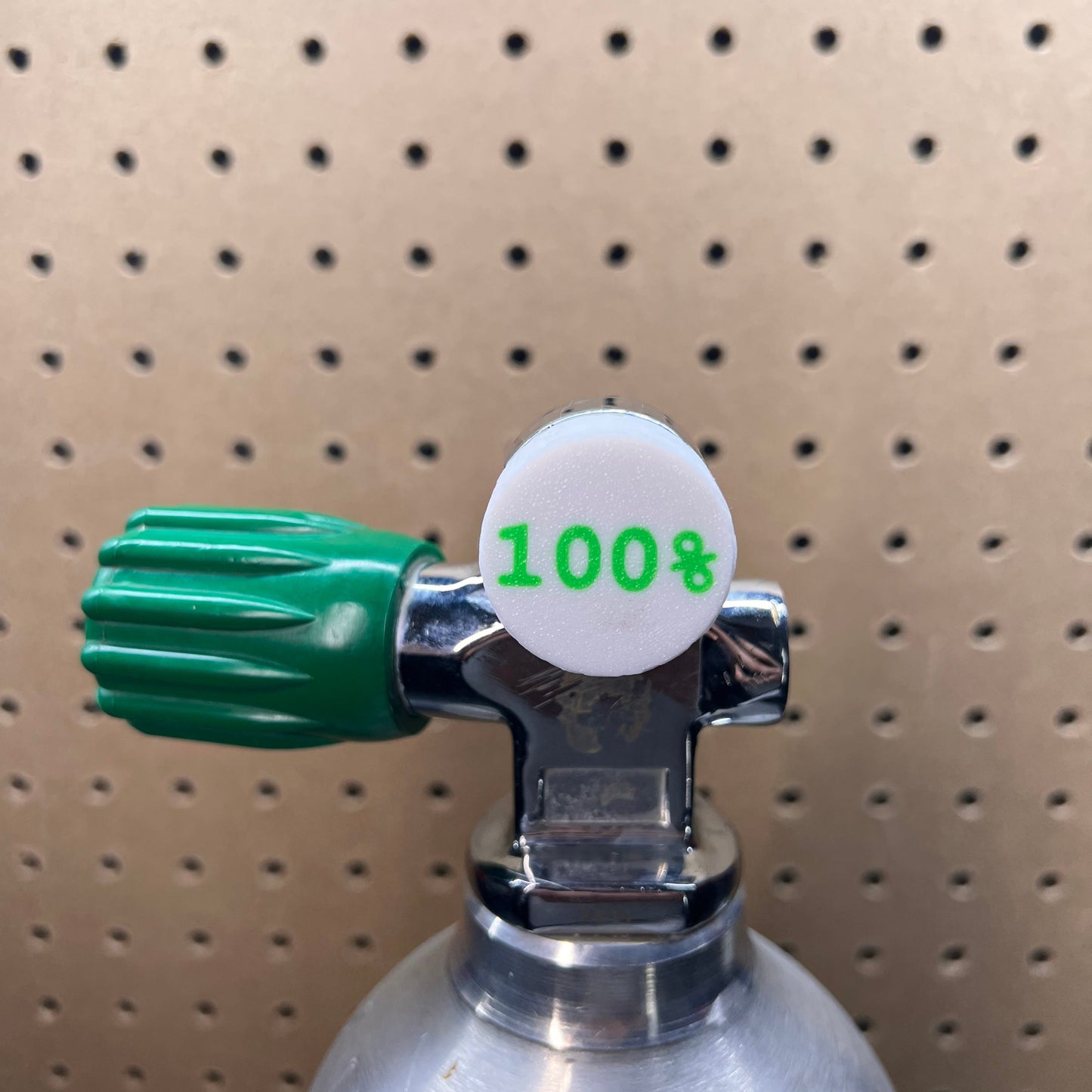 Close-up of a gas cylinder valve with a green handle on a pegboard background